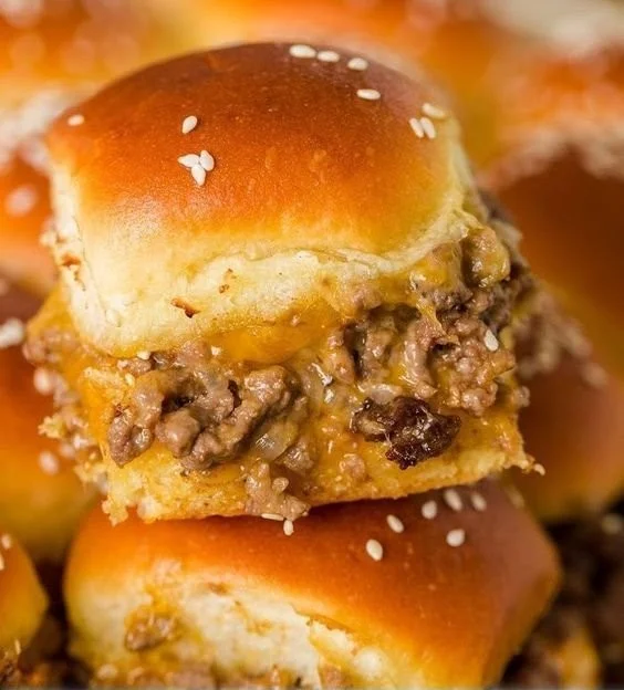 Golden cheeseburger sliders on a plate, garnished with pickles and cheese