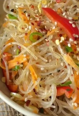 Colorful glass noodle salad with vegetables, herbs, and dressing in a bowl.