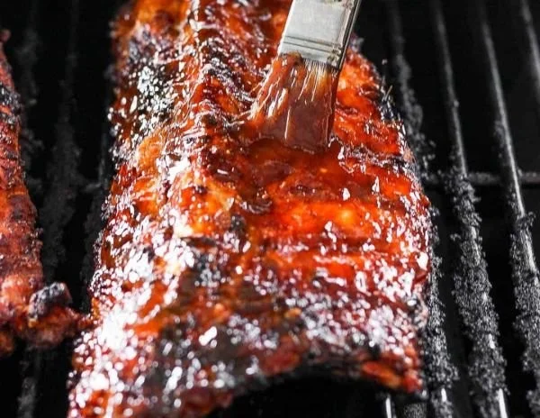 Delicious grilled ribs on a platter, garnished with herbs and BBQ sauce.