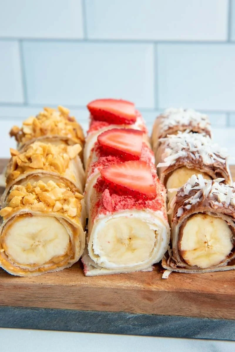 Tasty banana sushi rolls with fruit and nut toppings arranged on a plate.