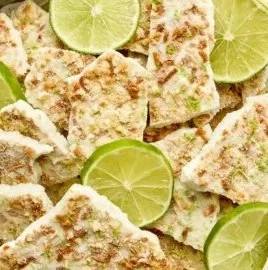 Key Lime Pie Yogurt Bark topped with lime zest and sliced limes on a marble surface.