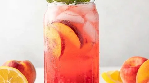 Refreshing Raspberry Peach Lemonade Cooler in a glass with ice and fruits