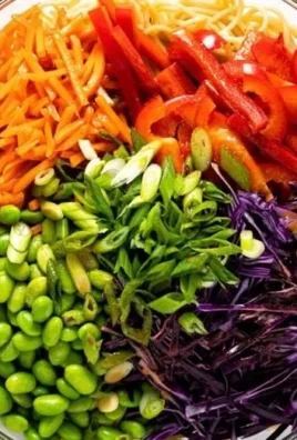 Bowl of vibrant sesame noodle salad topped with fresh vegetables and sesame seeds.