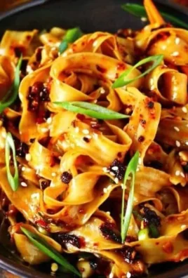 Bowl of spicy chili oil noodles garnished with green onions and sesame seeds