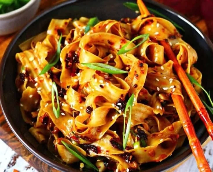 Bowl of spicy chili oil noodles garnished with green onions and sesame seeds