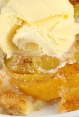 Freshly baked homemade peach cobbler served in a dish with a scoop of ice cream.