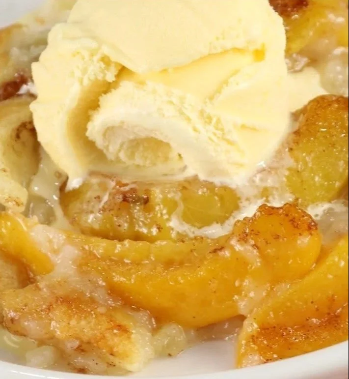 Freshly baked homemade peach cobbler served in a dish with a scoop of ice cream.