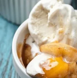 Individual peach cobbler served in a ramekin with vanilla ice cream on top
