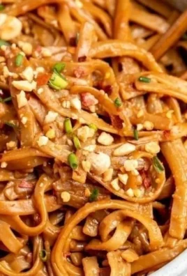 Bowl of spicy peanut butter noodles garnished with vegetables and herbs