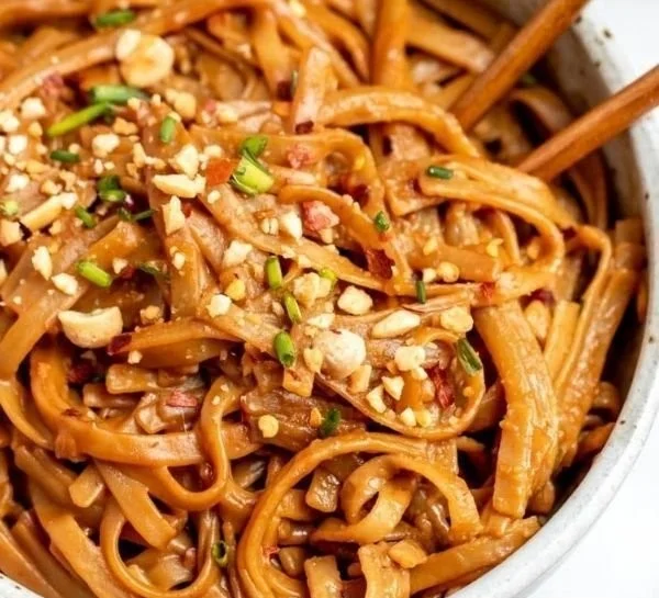 Bowl of spicy peanut butter noodles garnished with vegetables and herbs