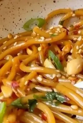 Bowl of spicy sesame noodles garnished with green onions and sesame seeds.