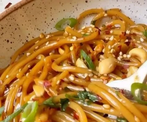 Bowl of spicy sesame noodles garnished with green onions and sesame seeds.