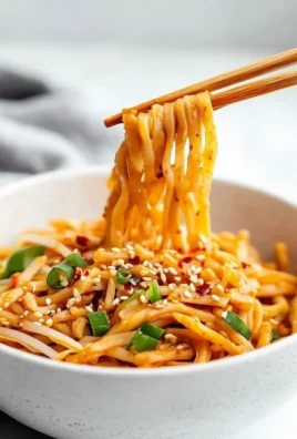Bowl of sweet and spicy noodles topped with fresh herbs and vegetables