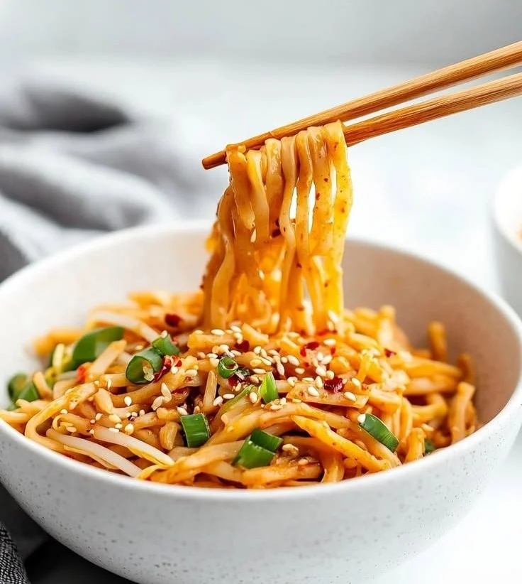 Bowl of sweet and spicy noodles topped with fresh herbs and vegetables