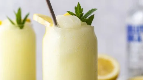 Boozy frozen lemonade served in a glass with lemon slices and ice.