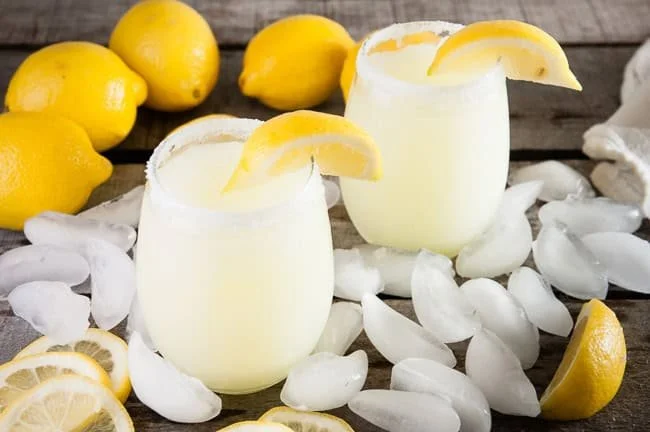 Refreshing boozy lemonade slushies in colorful glasses with fruit garnishes.