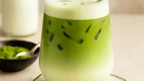 Iced matcha latte in a glass with green tea powder and milk.