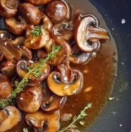 Plate of pan-seared mushrooms with caramelized shallots and thyme garnish.