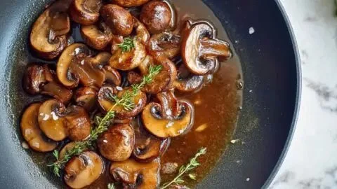 Plate of pan-seared mushrooms with caramelized shallots and thyme garnish.