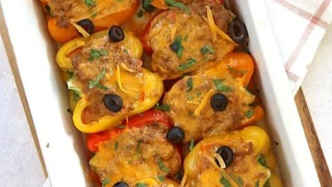 Stuffed taco peppers with ground meat and cheese topped with herbs in a dish