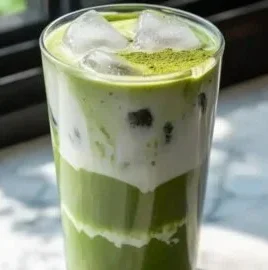 Homemade iced vanilla matcha latte with whipped cream and vanilla beans