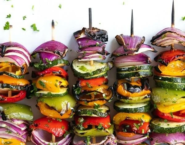Colorful veggie skewers with bell peppers, zucchini, and mushrooms on a grill.